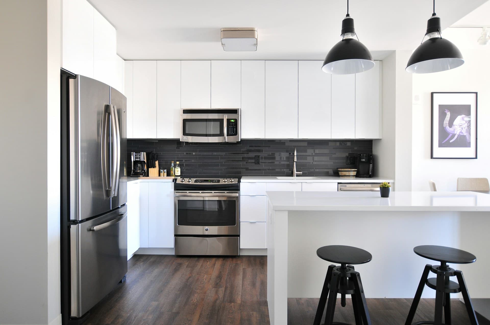 Bright kitchen with white cabinets, stainless steel appliances, pendant lighting, and a breakfast bar.